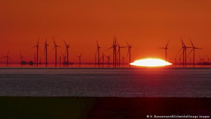 The sun rises over a series of wind turbines on the coast in Schleswig-Holstein